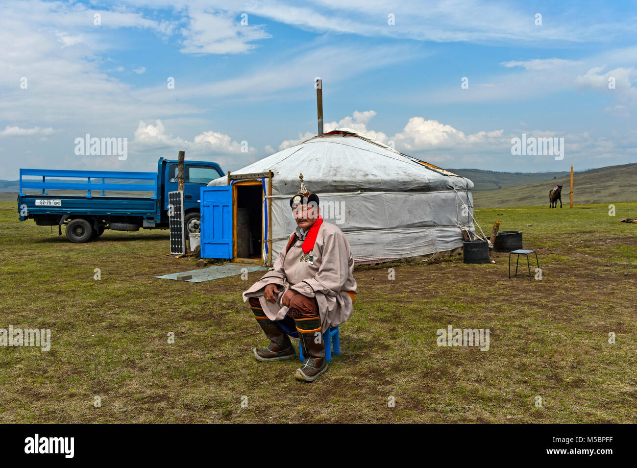 Elderly male nomad in traditional dress sitting in front of his yurt ...