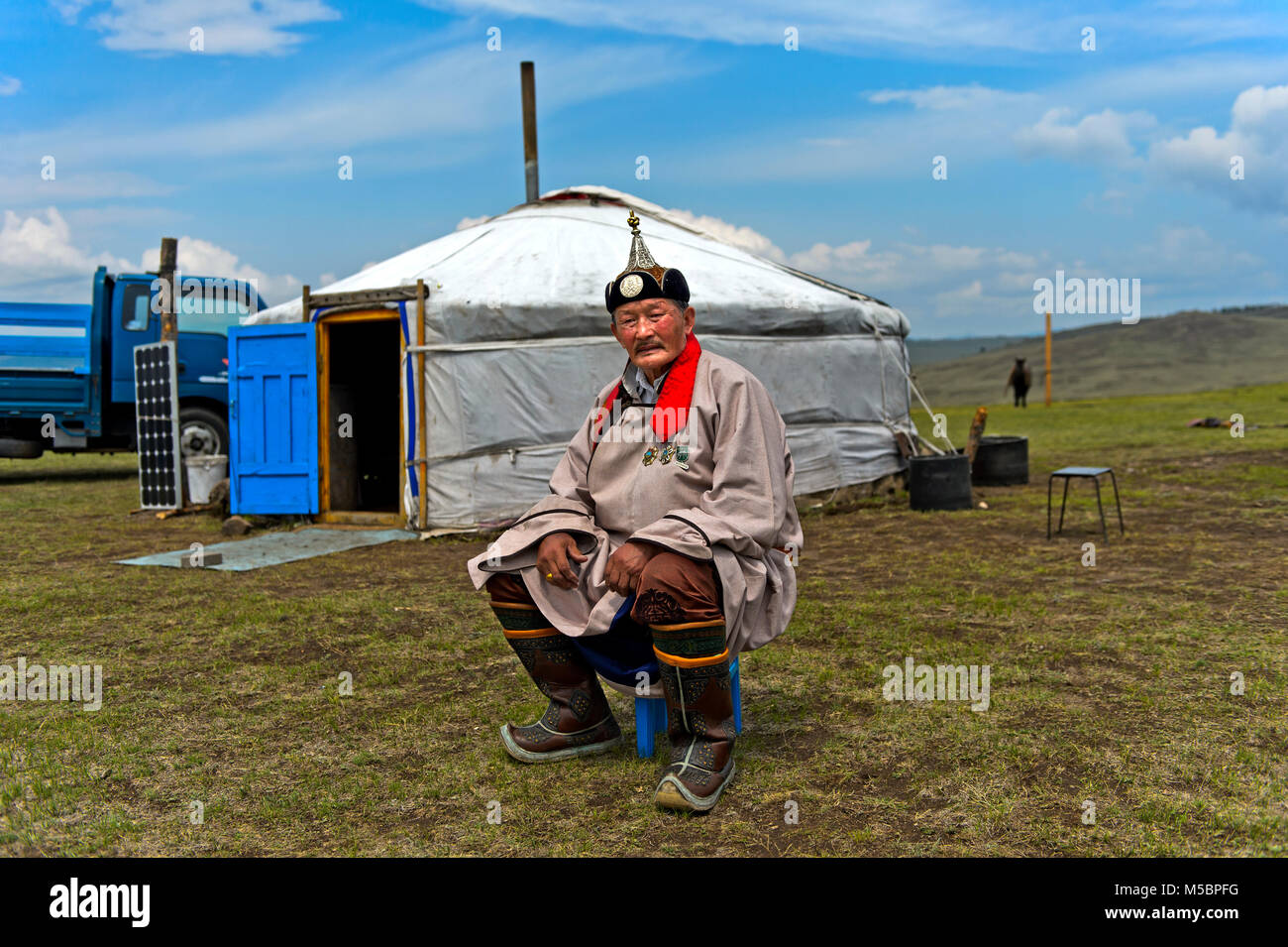 Elderly male nomad in traditional dress sitting in front of his yurt, Mongolia Stock Photo