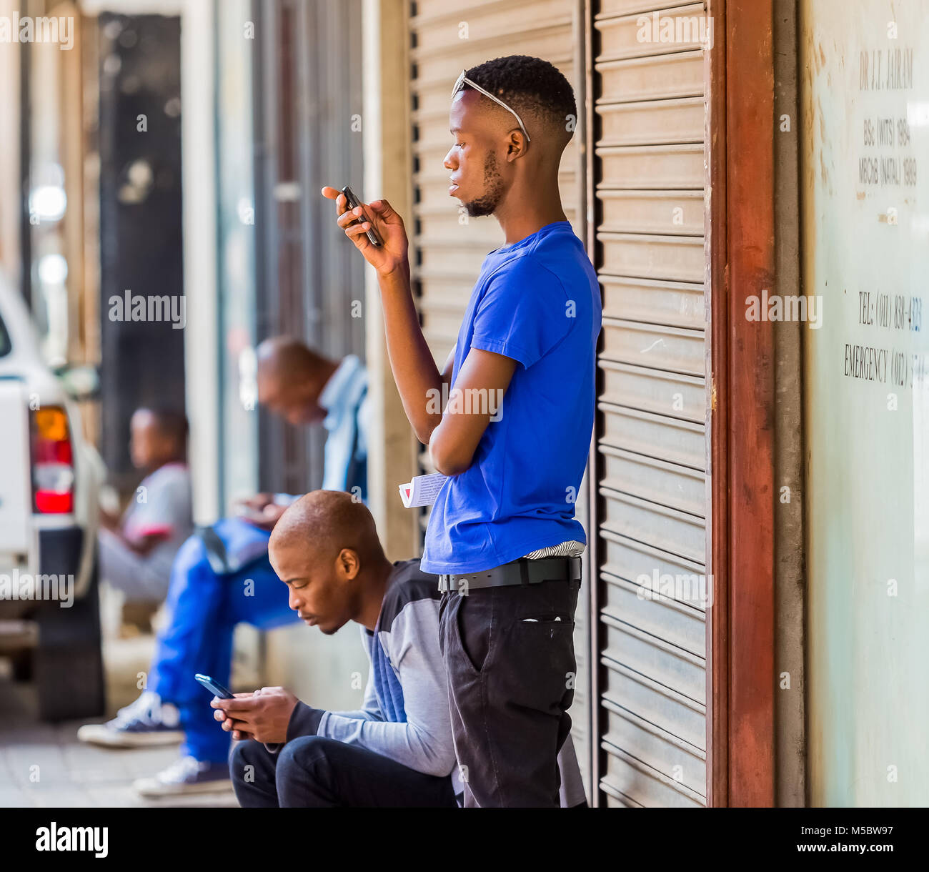 African men using their mobile phones on a side walk in a busy city Stock Photo
