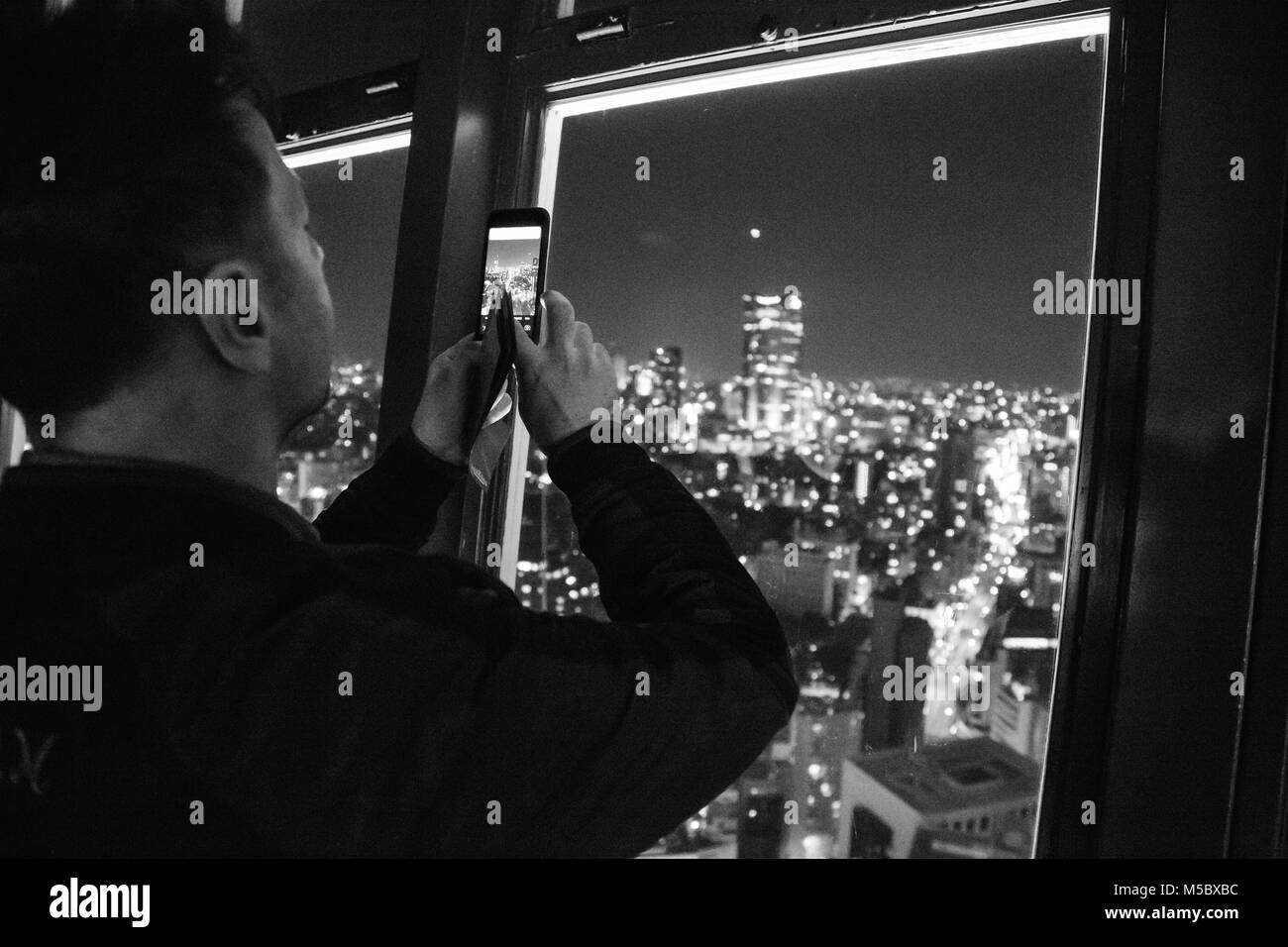 A caucasian man photographs views of the Tokyo cityscape and skyline at night, from atop Tokyo Tower in Tokyo. Stock Photo