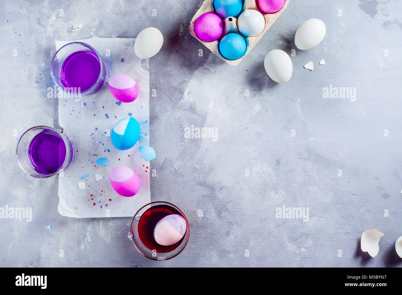 Easter eggs painting in progress. Shades of blue, pink and purple. Top view with copy space. Holiday decorations on a white concrete background. Stock Photo