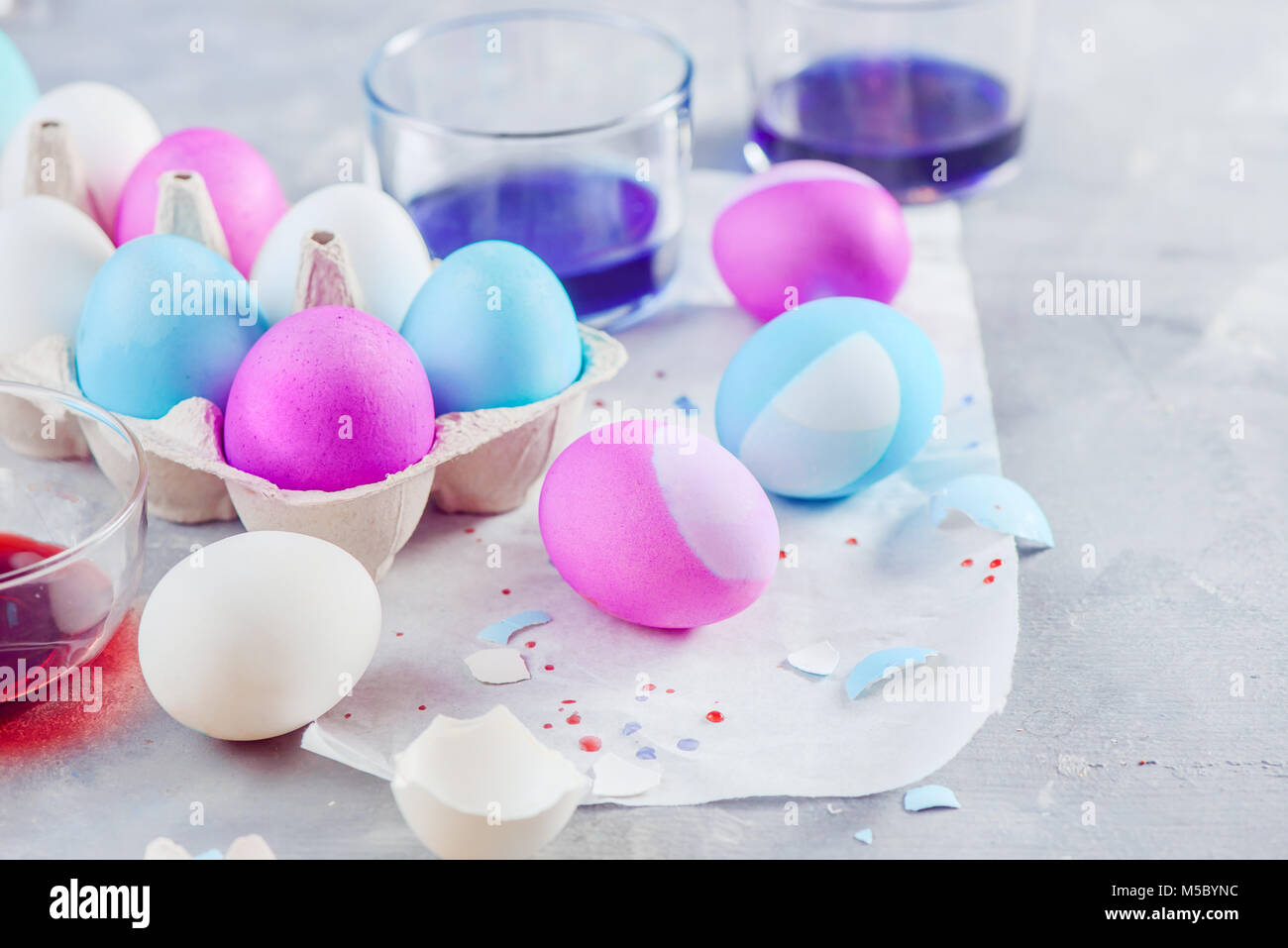 Close-up of Easter eggs painting in progress. Shades of blue, pink and purple. Holiday decorations on a white concrete background. Stock Photo