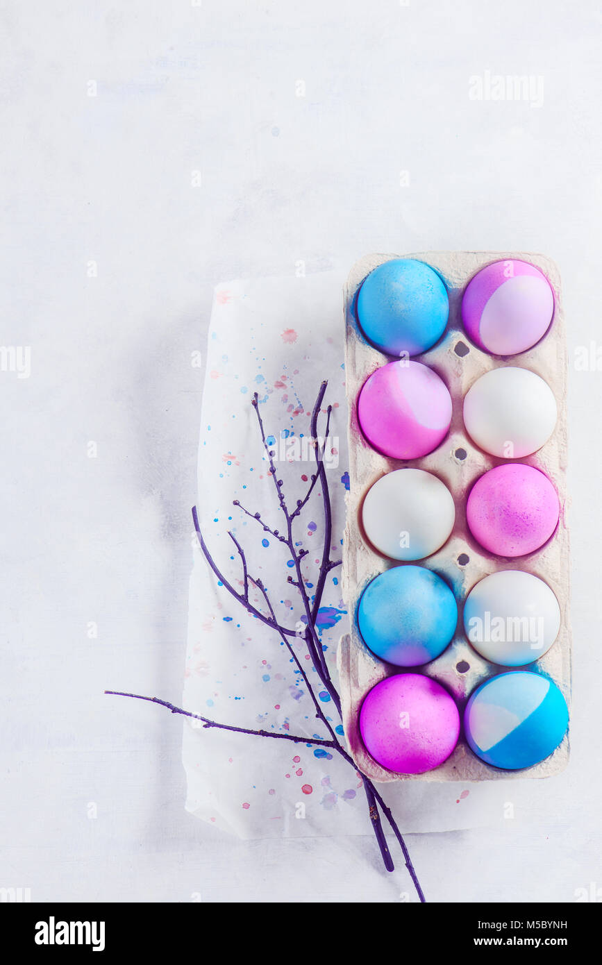 Easter eggs painted in blue and purple shades in a carton with tree branches and copy space. Minimalist Easter concept. View from above. Stock Photo