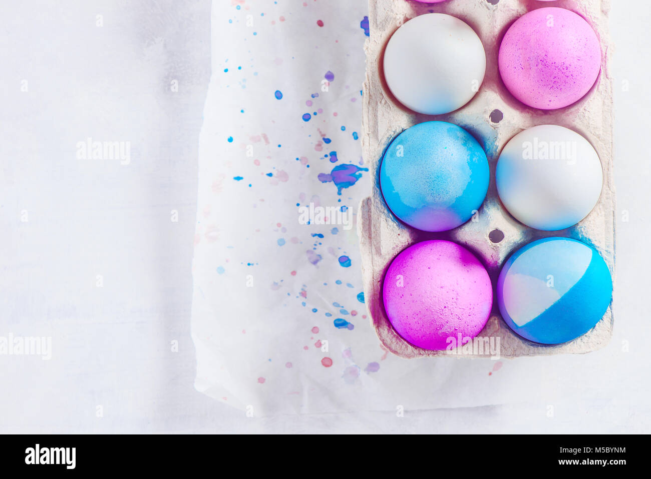 Easter eggs painted in blue and pink shades in a carton with drops of dye. Modern Easter concept with copy space. Concrete background from above. Stock Photo