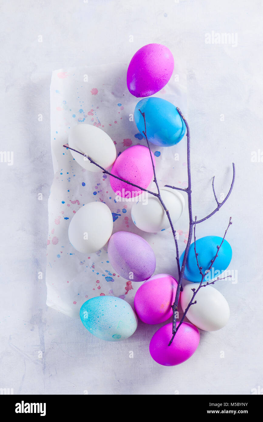 Easter eggs in a high key scene with a tree branch. A minimalist concept from above. Shades of blue, pink and purple. Stock Photo