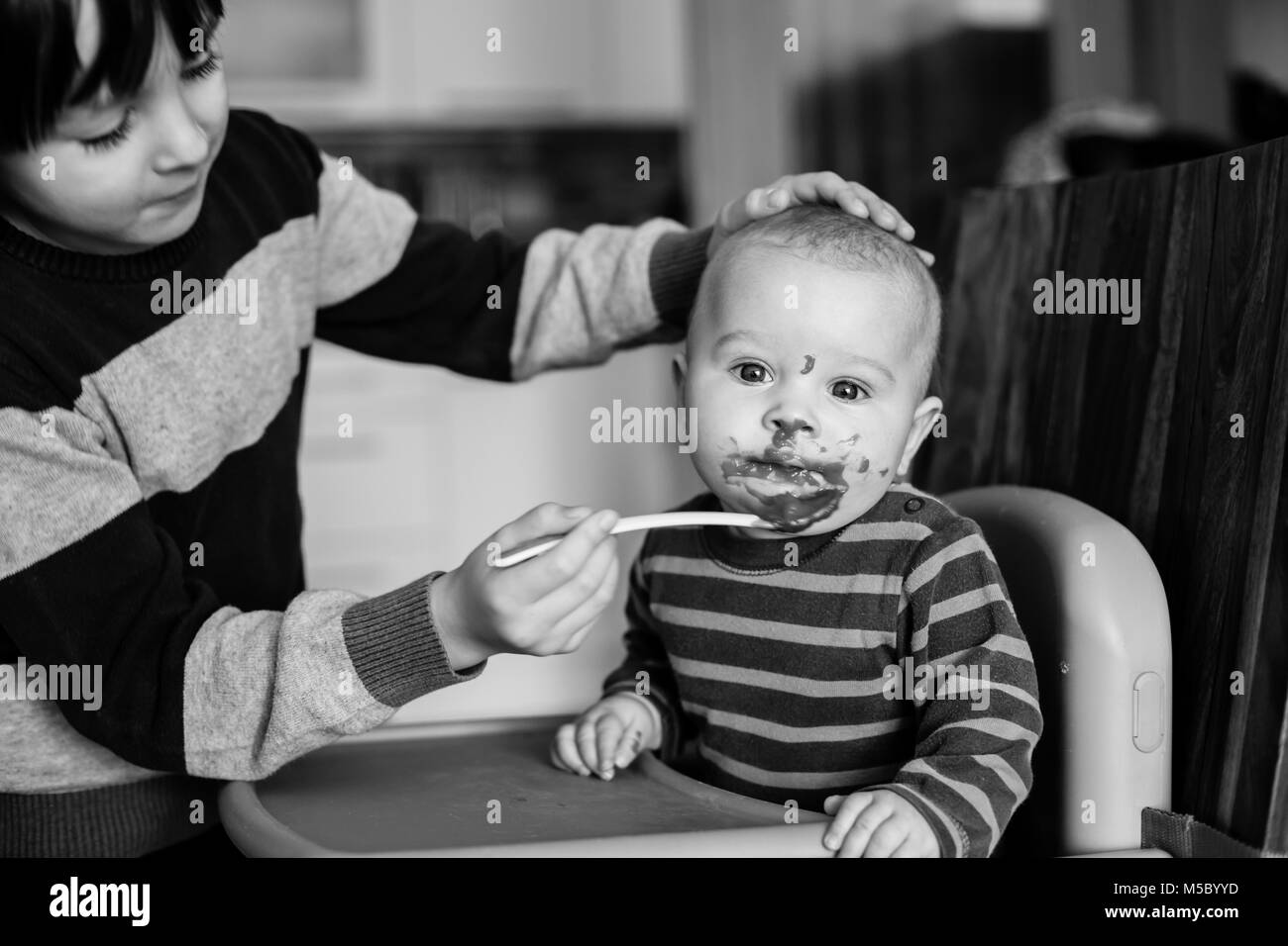 Cute preschool boy, feeding his baby brother with mashed vegetables, baby eating mashed food for the first time Stock Photo