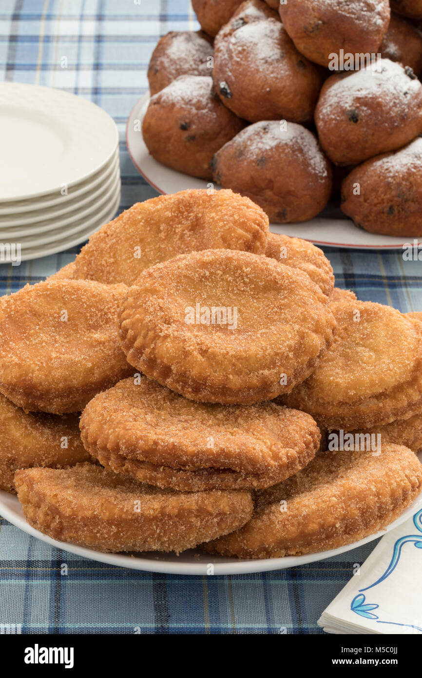 Dish with  sugared fried apple fritters or appelflappen and a dish with oliebollen on the background, traditional Dutch pastry for New Year's Eve Stock Photo