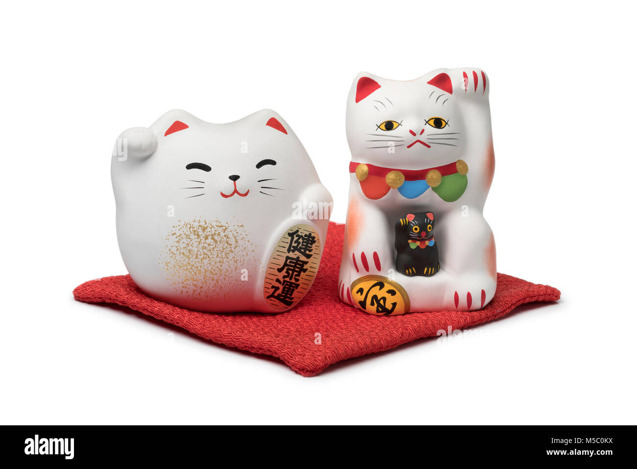 Japanese maneki neko, lucky cats on a red pillow isolated on white background Stock Photo