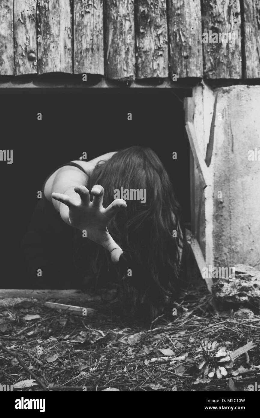 Scene of terror, girl on the ground with hair on her face with her arm outstretched crawling out of a basement Stock Photo