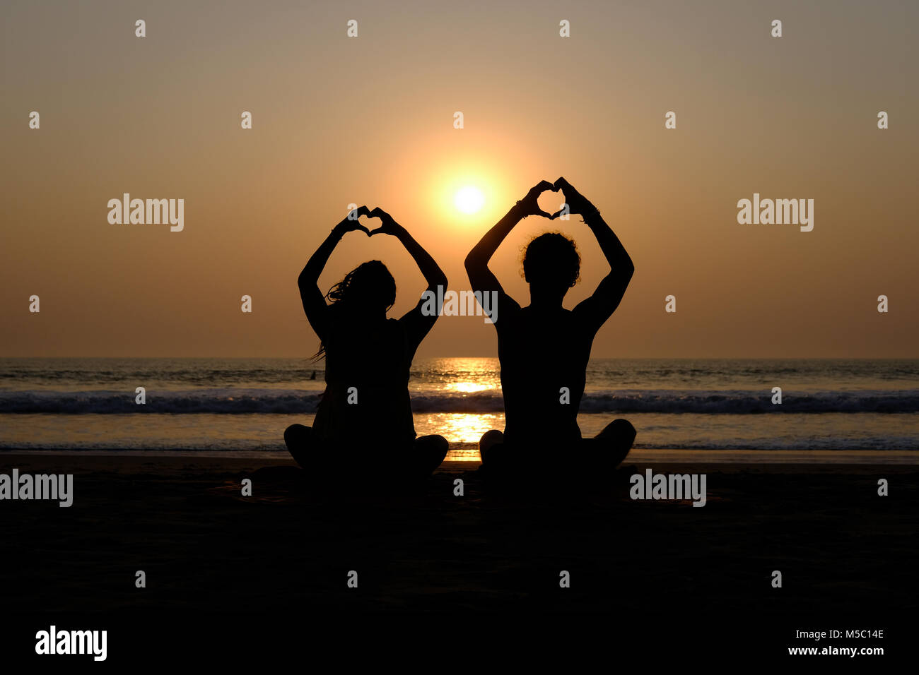 Couple's silhouette drawing hearts with their hands on the beach at sunset, Gokarna (Karnataka, India) Stock Photo
