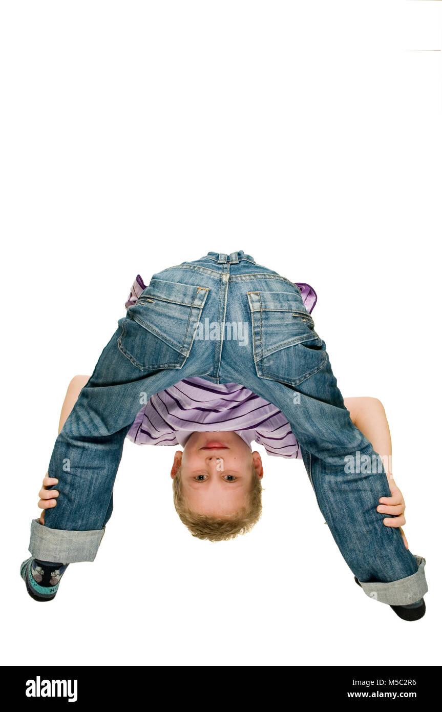 Boy standing with his back to the camera, standing in front of him, bending over his pawed legs towards the camera smiling against white background. Stock Photo