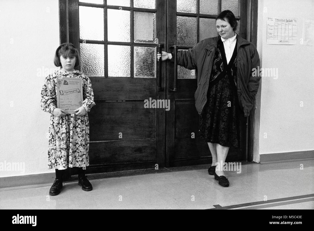 Young girl holding prize certificate as lady keeps door closed at small eisteddfod in village hall at Llandudoch St Dogmaels Dyfed West Wales UK Stock Photo