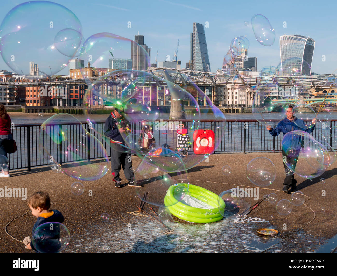 buskers blow bubbles along south bank with city behind Stock Photo