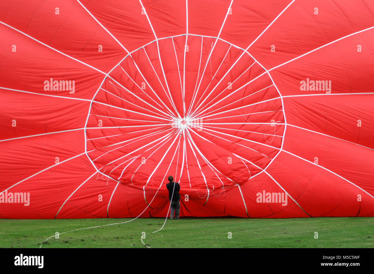 A young man holds on to the rigging of a hot air balloon while it is being inflated before a balloon flight Stock Photo