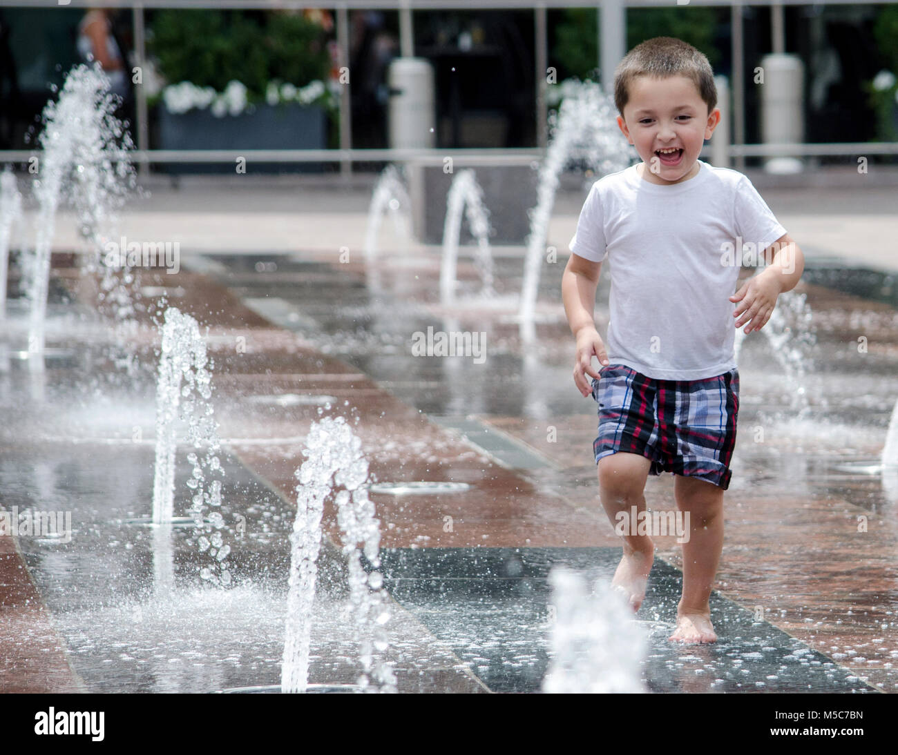 a gleeful little boy splashes in a city splash pad in Denver CO USA Stock Photo