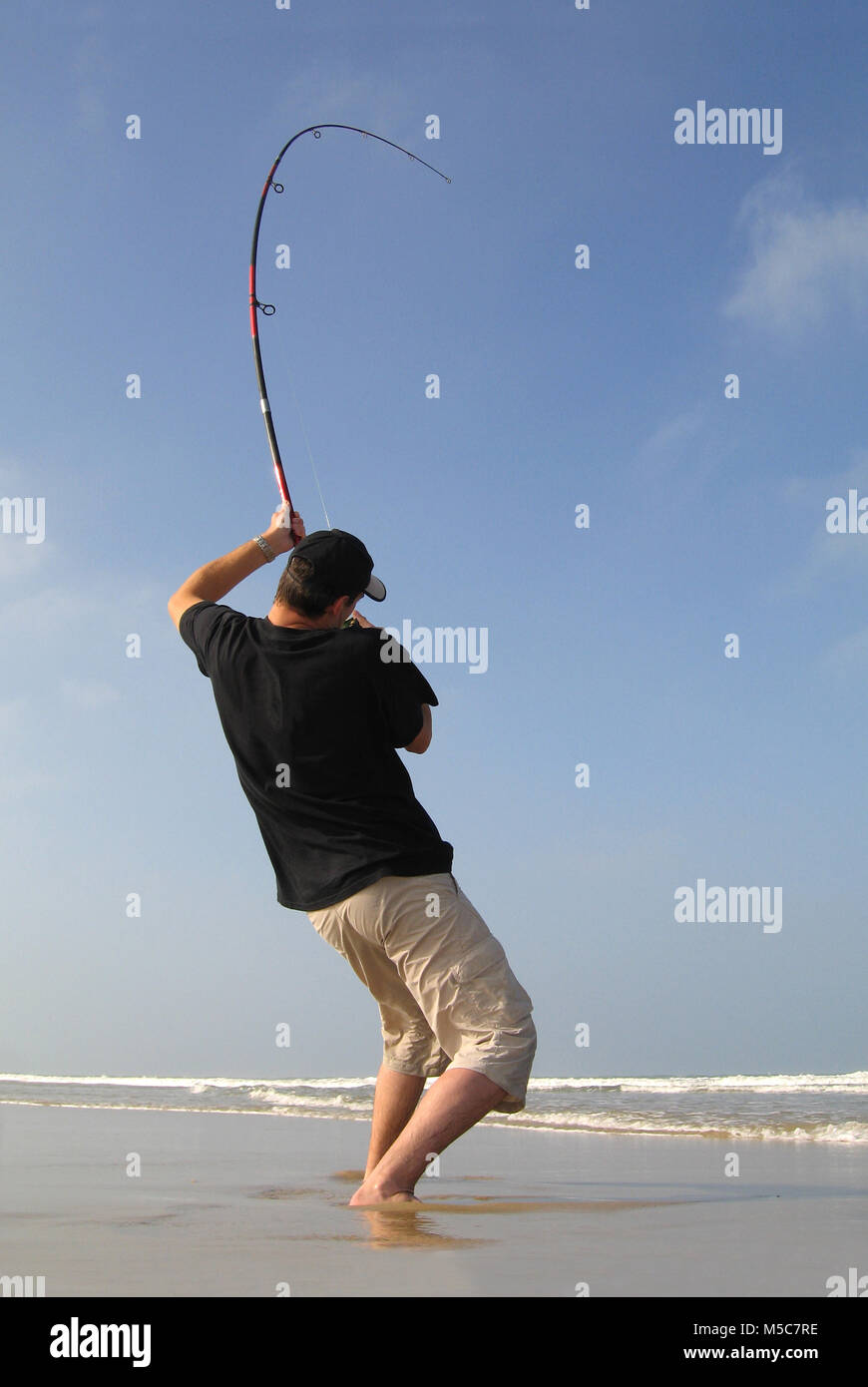Surf fisherman fighting a fish on a beach, fishing scene. the rod is