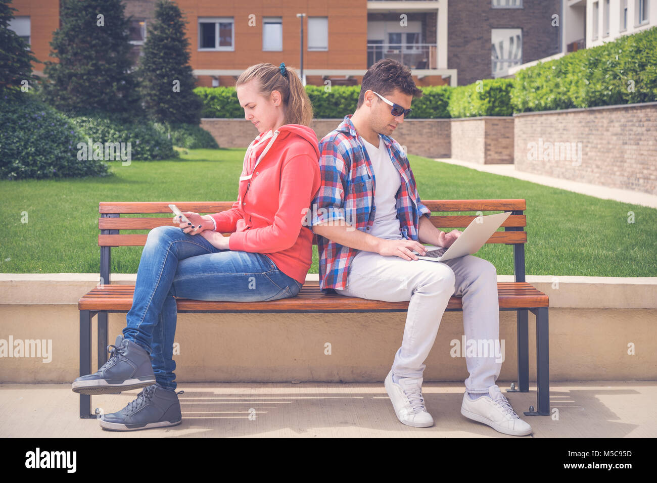 Beautiful young couple sitting on bench in the park and using modern ...
