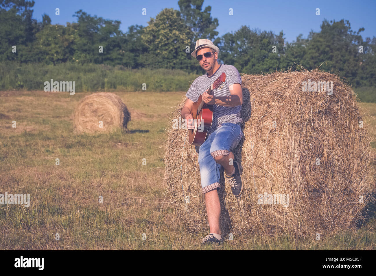 Portrait of stylish man playing acoustic guitar in nature. Stock Photo