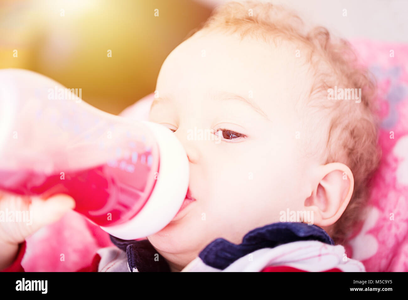 Cute baby drinking water from bottle sitting on chair. Close up
