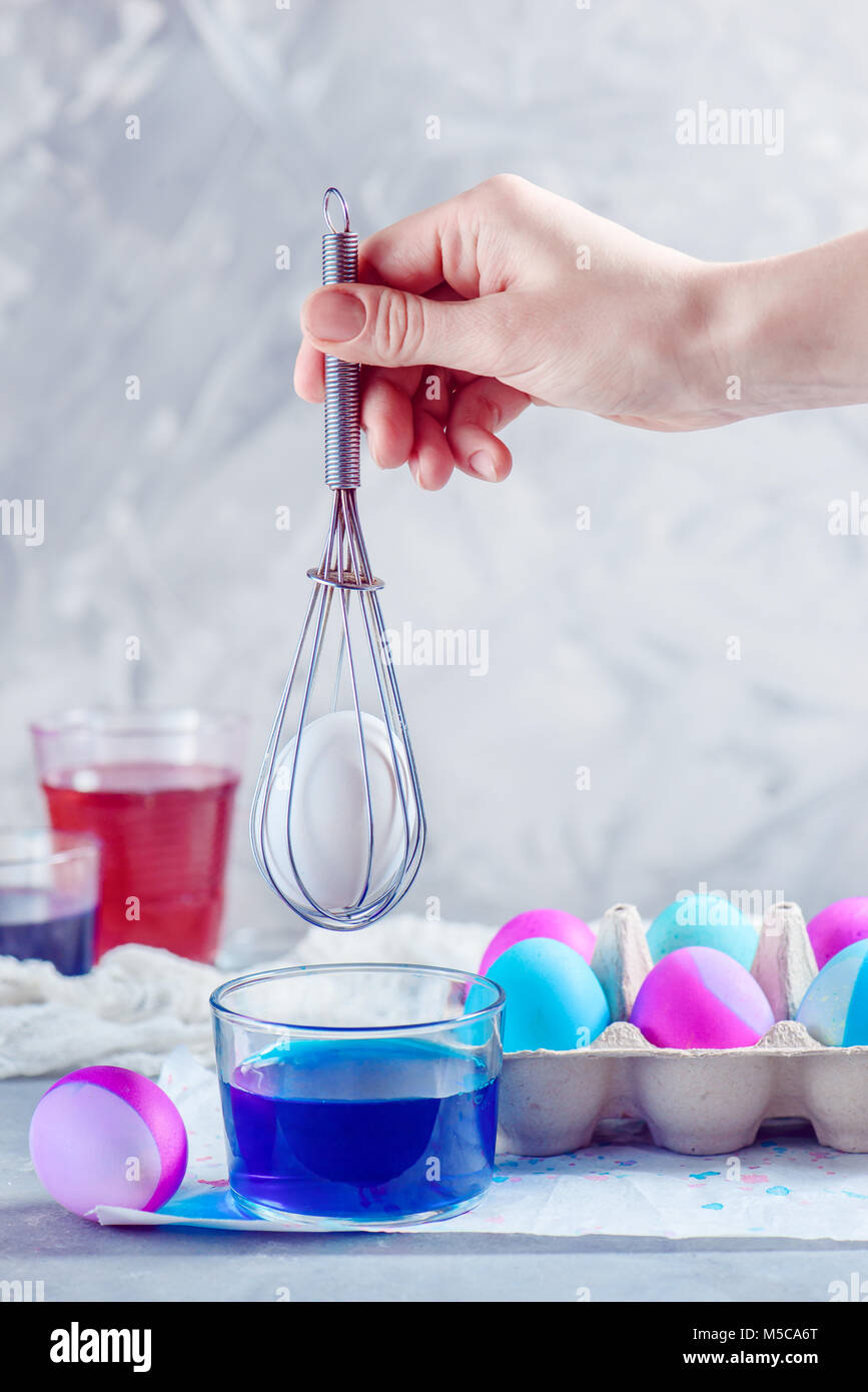 Woman hand painting Easter eggs with a whisk. Modern holiday decorations with copy space. Stock Photo
