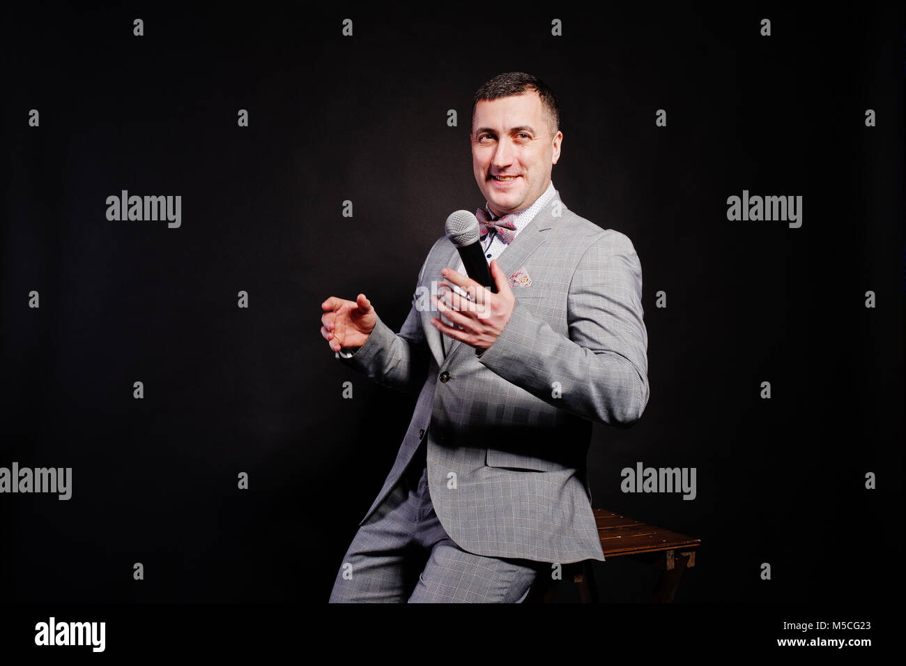 Toastmaster Microphone Handsome man in gray suit with microphone against black background on ...