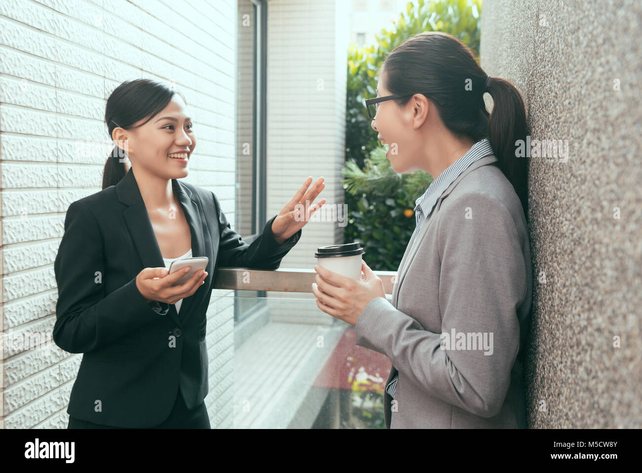 two Asian women talking funny things together and have coffee for afternoon tea at outdoor of the studio office. Stock Photo