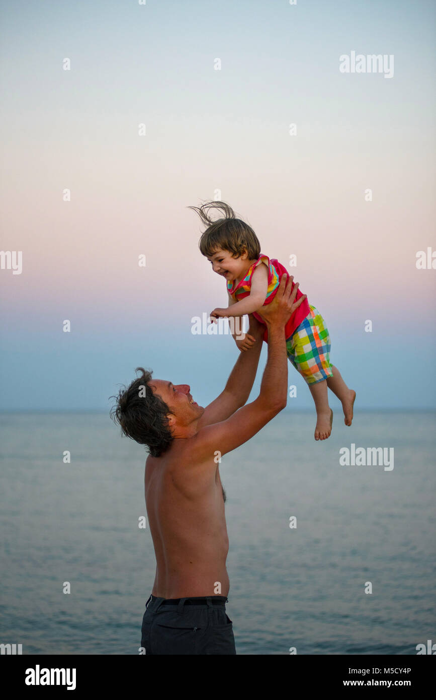 Quality time concept. Young father having fun and throwing her daughter in the air at sunset. Summer vacation at sea Stock Photo