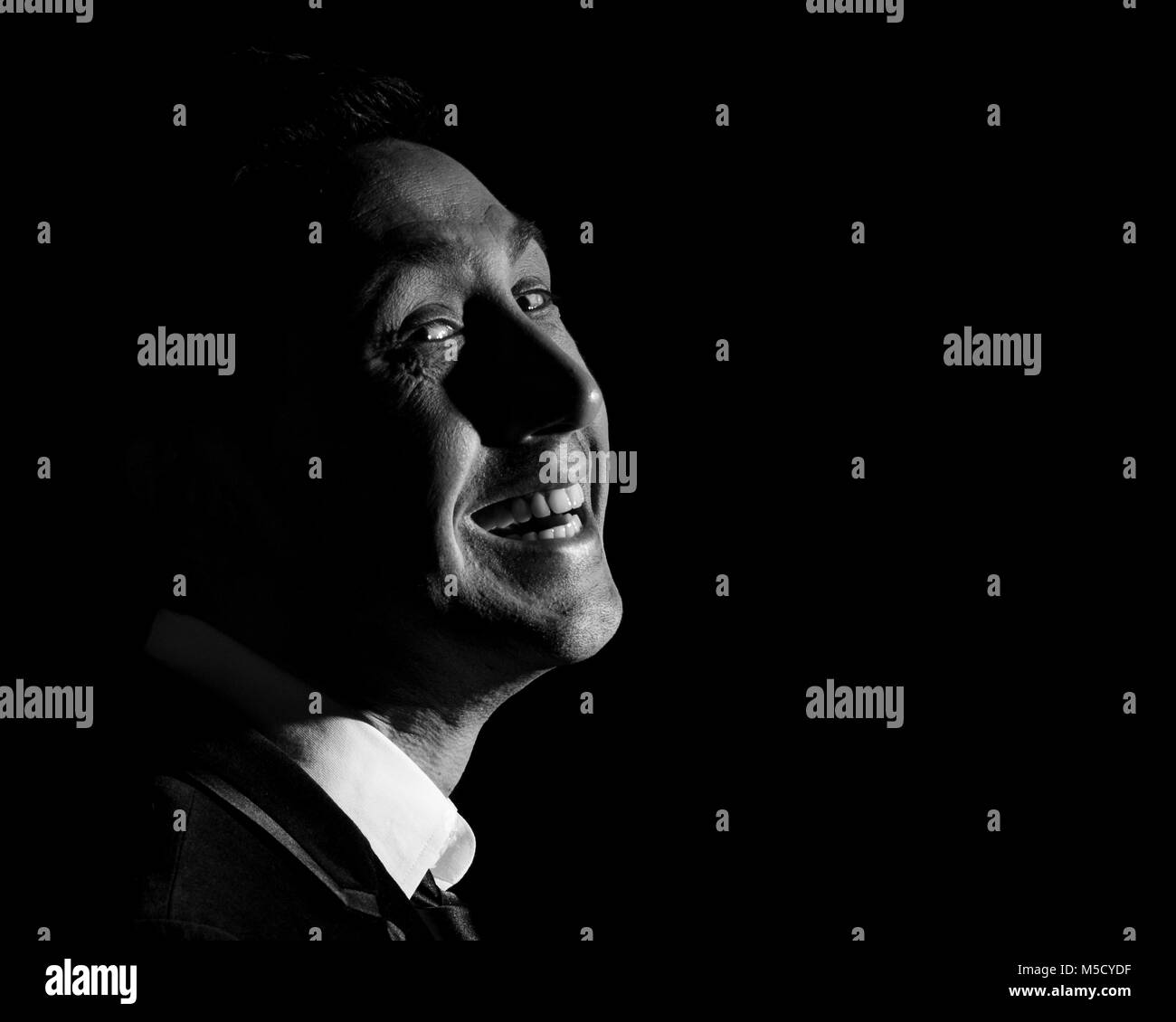 Portrait of man in his thirties with a scary grin on a black background Stock Photo