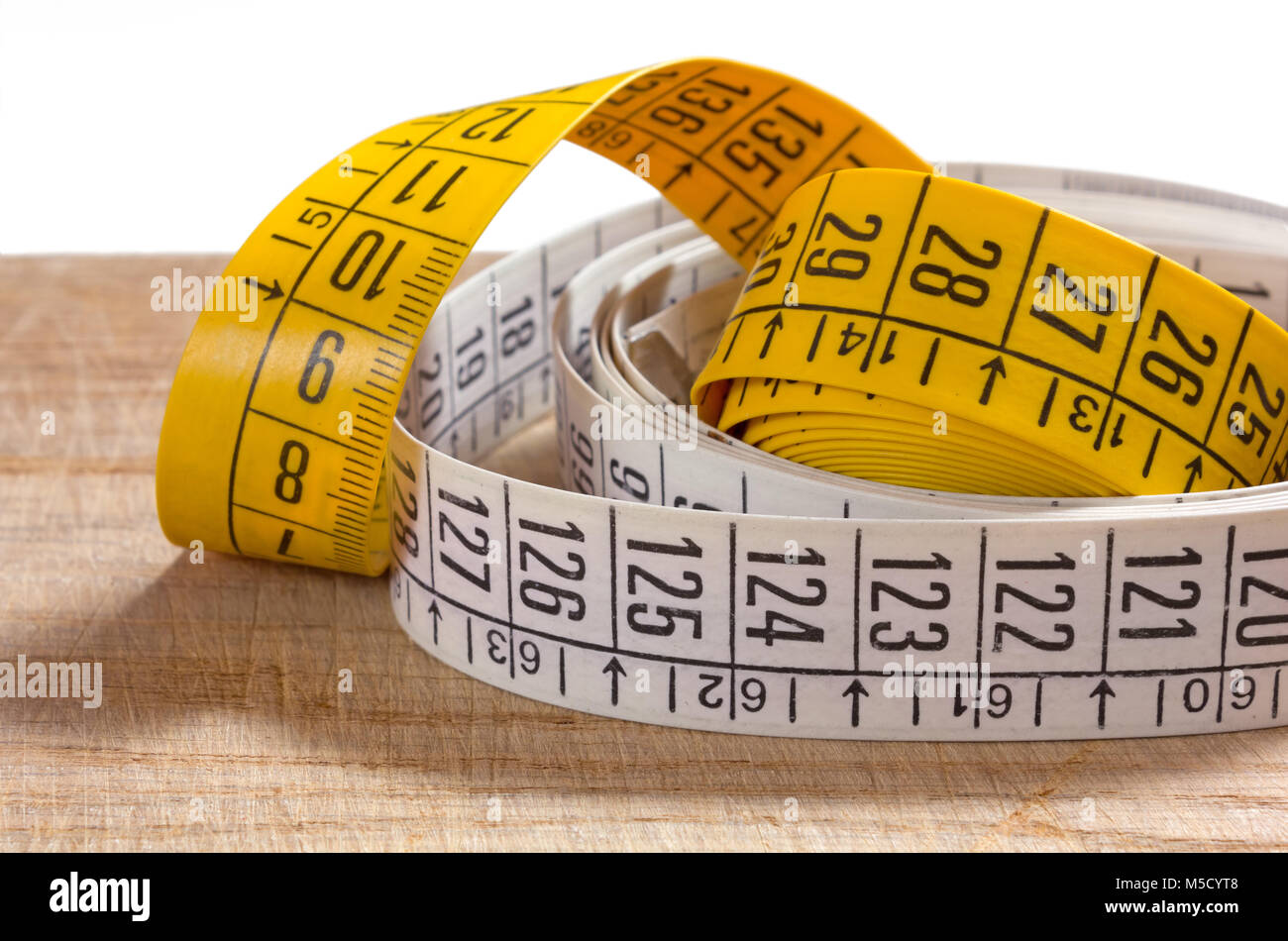 Two rolled-up white and yellow tailor measuring tape on an old wooden  surface Stock Photo - Alamy