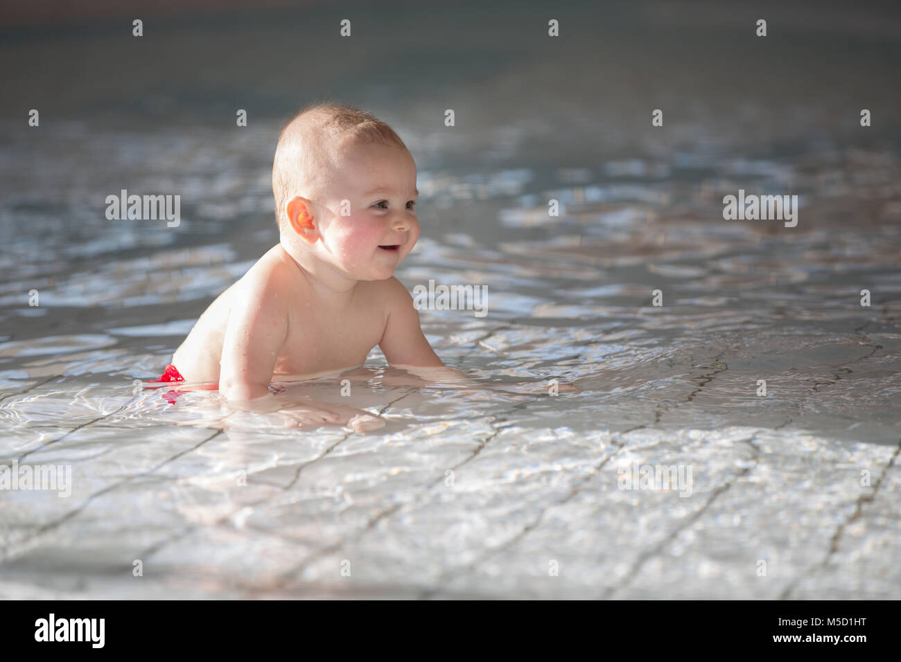 Little cute baby boy, swimming happily in a shallow pool, splashing