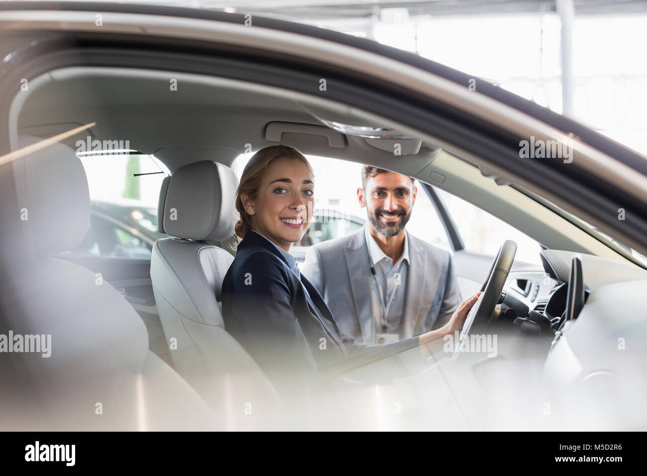 Portrait smiling woman and car salesman sitting in new car at car dealership Stock Photo