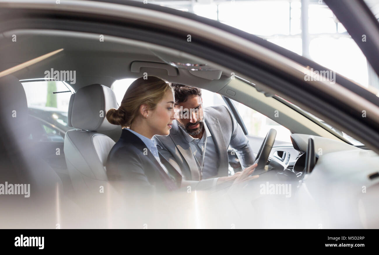 Car salesman showing new car to woman in driver’s seat at car dealership Stock Photo