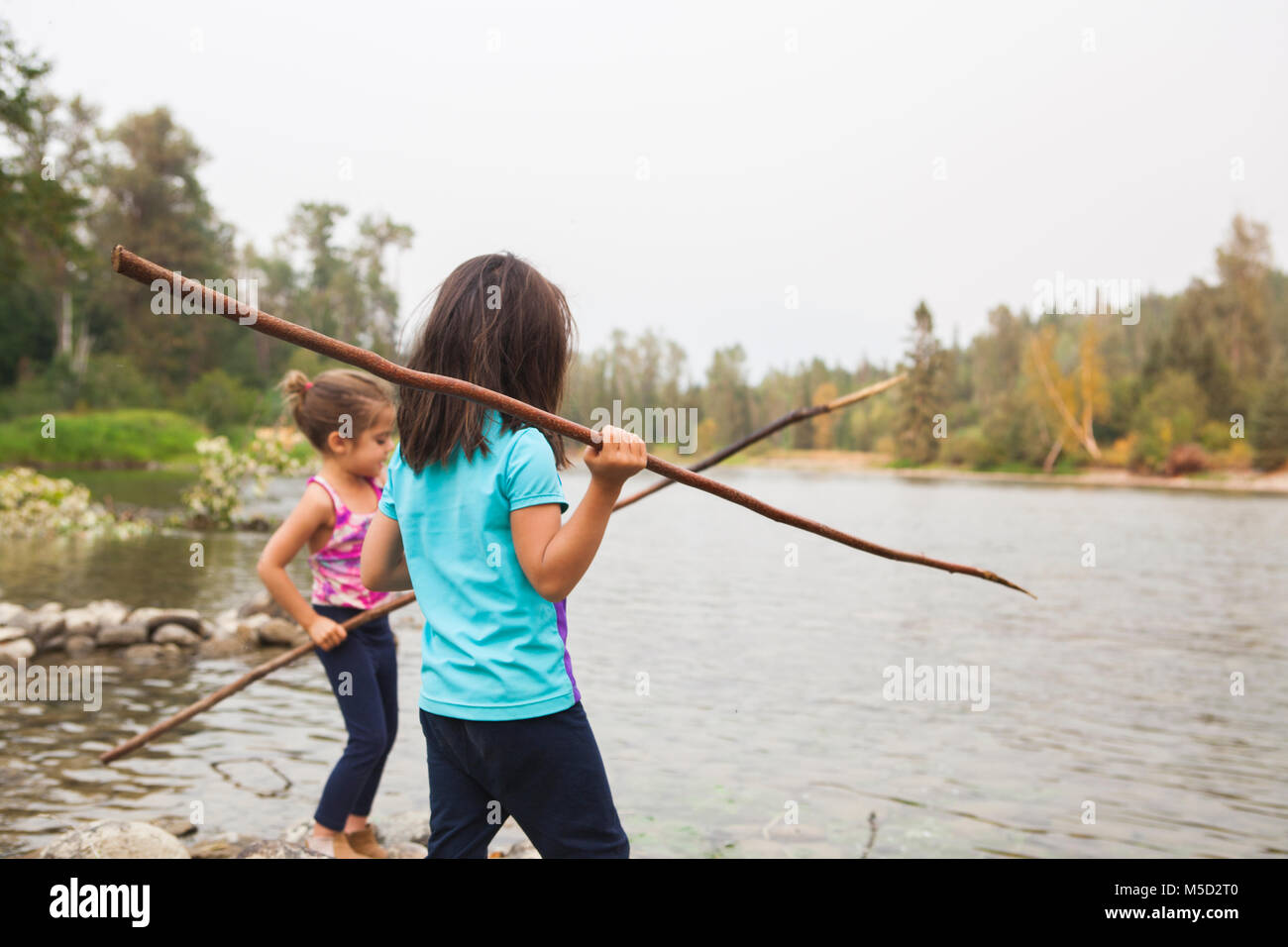 Girls fishing with sticks at lake Stock Photo