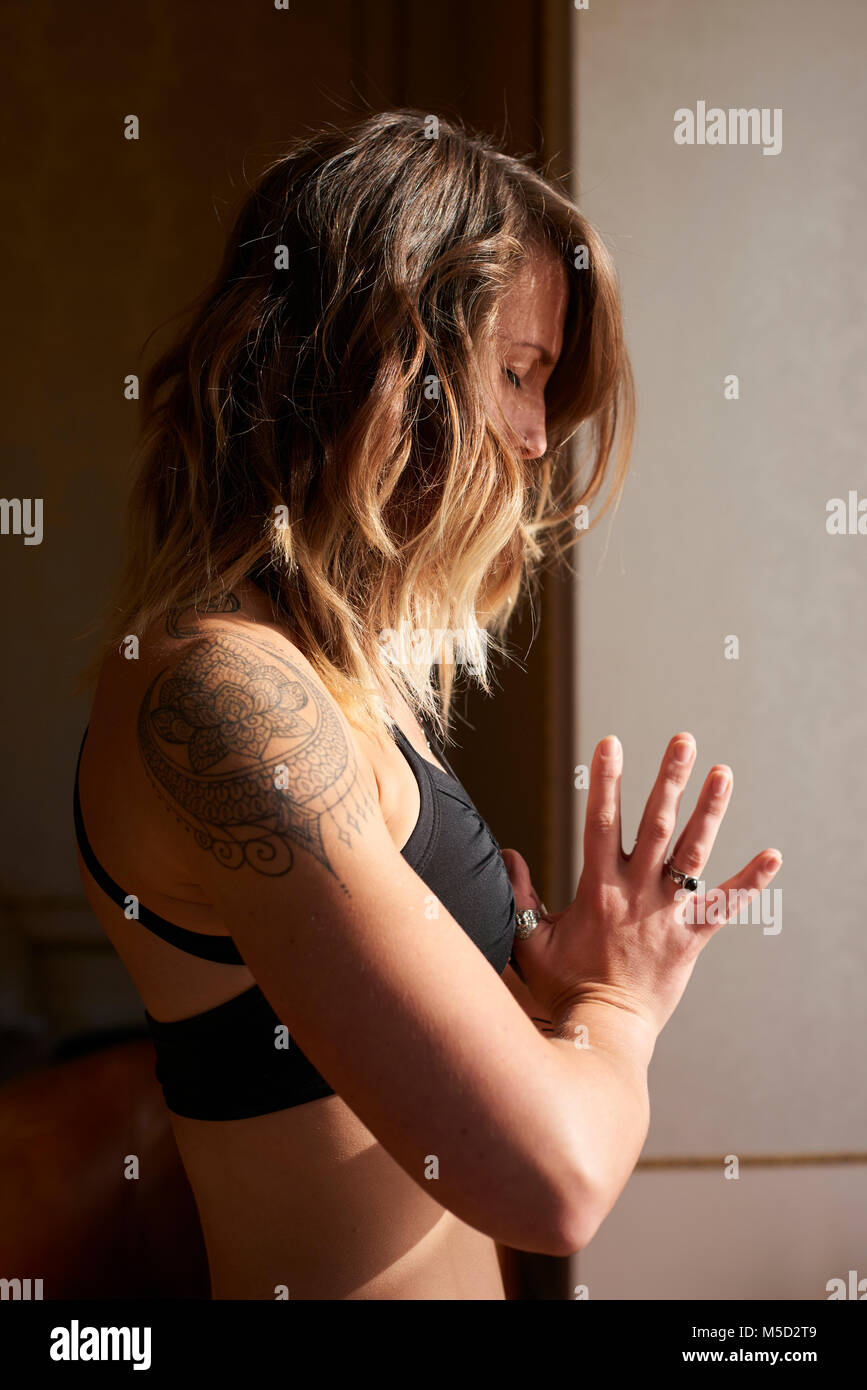 Serene woman with tattoo meditating with hands at heart center, anjali mudra Stock Photo