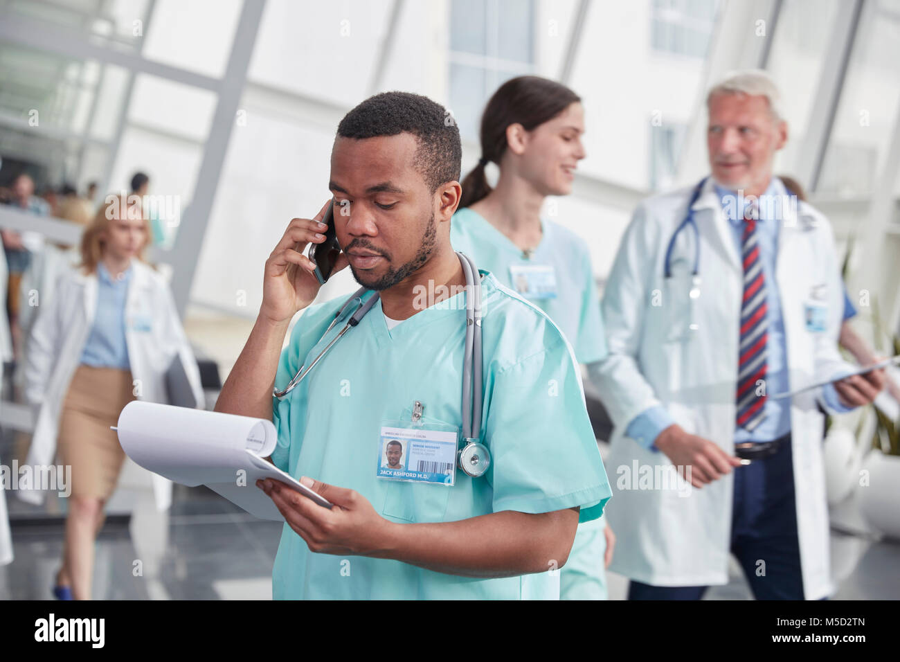 Male nurse with clipboard talking on cell phone in hospital corridor Stock Photo