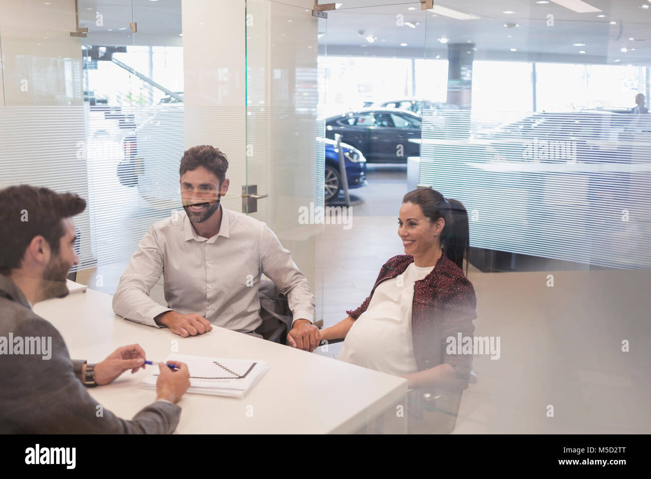 Car salesman talking to pregnant couple in car dealership office Stock Photo