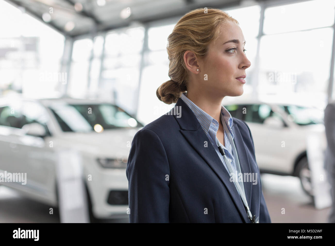 Pensive car saleswoman looking away in car dealership showroom Stock Photo