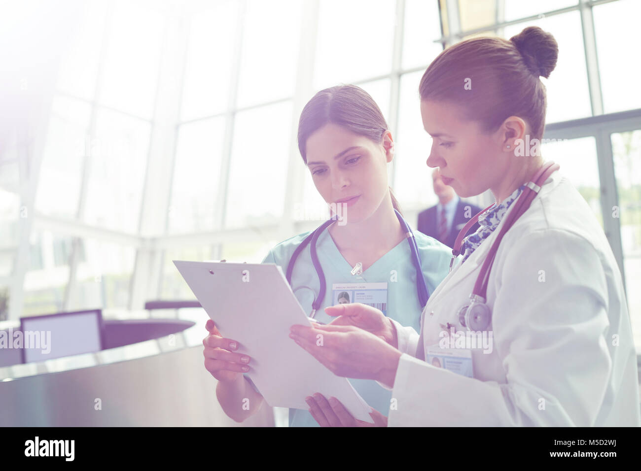 Female doctor and nurse consulting, reviewing medical record on clipboard in hospital Stock Photo