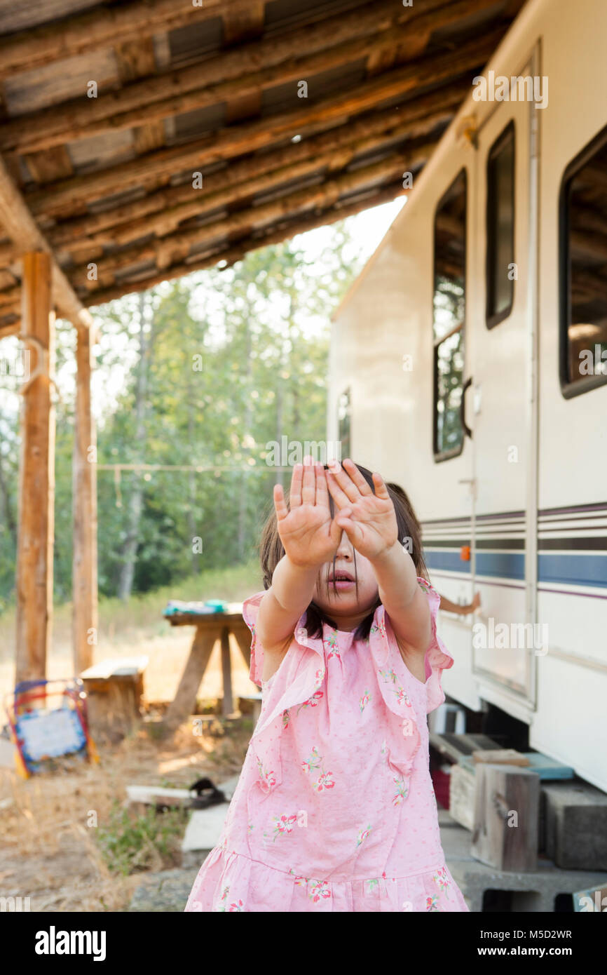 Portrait shy girl hiding face with hands outside rural camper Stock Photo