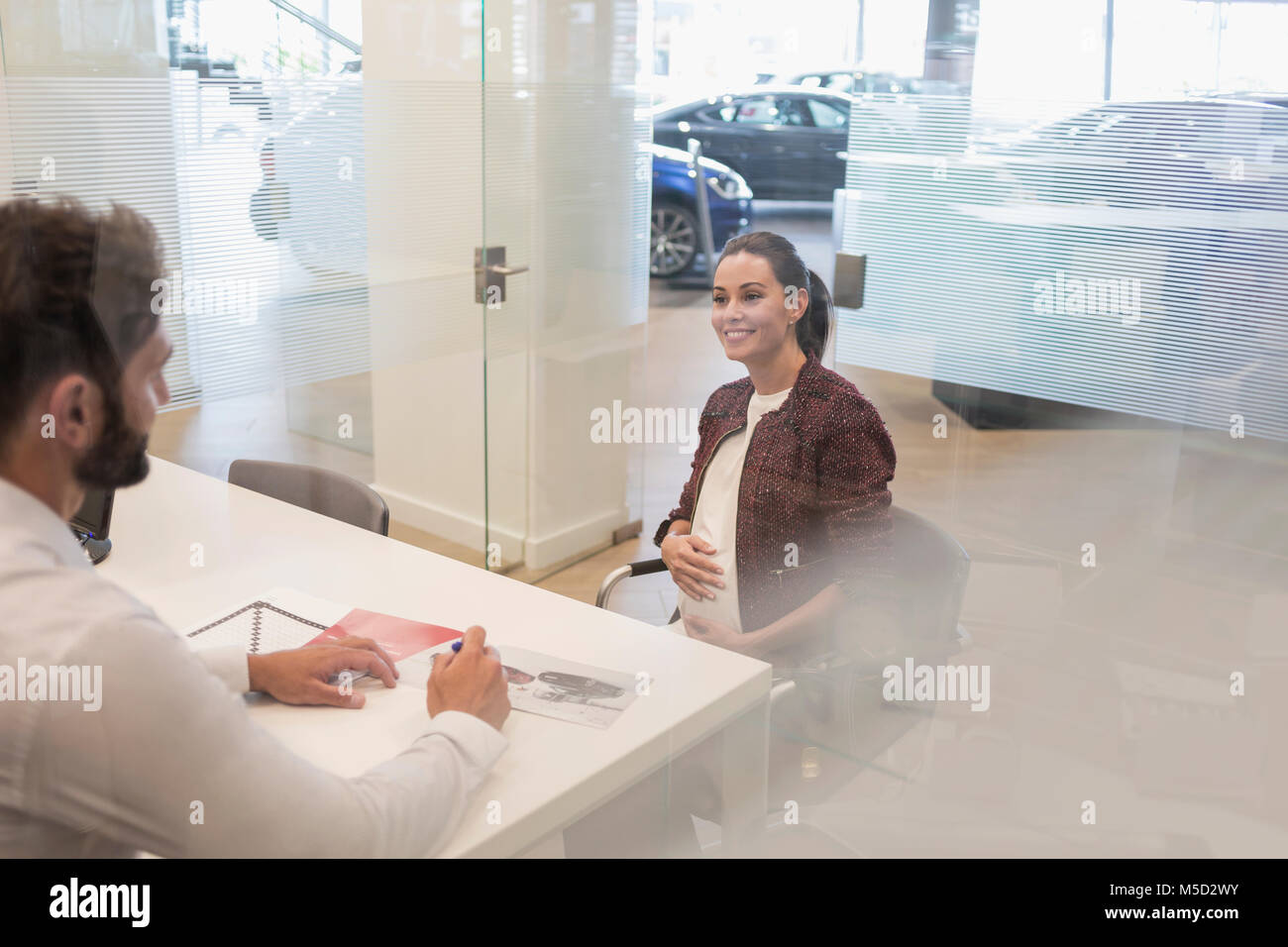 Car salesman talking to pregnant customer in car dealership office Stock Photo