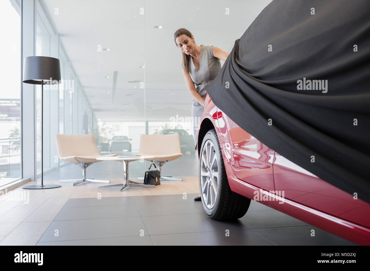 Car saleswoman removing cover from new car in car dealership showroom Stock Photo