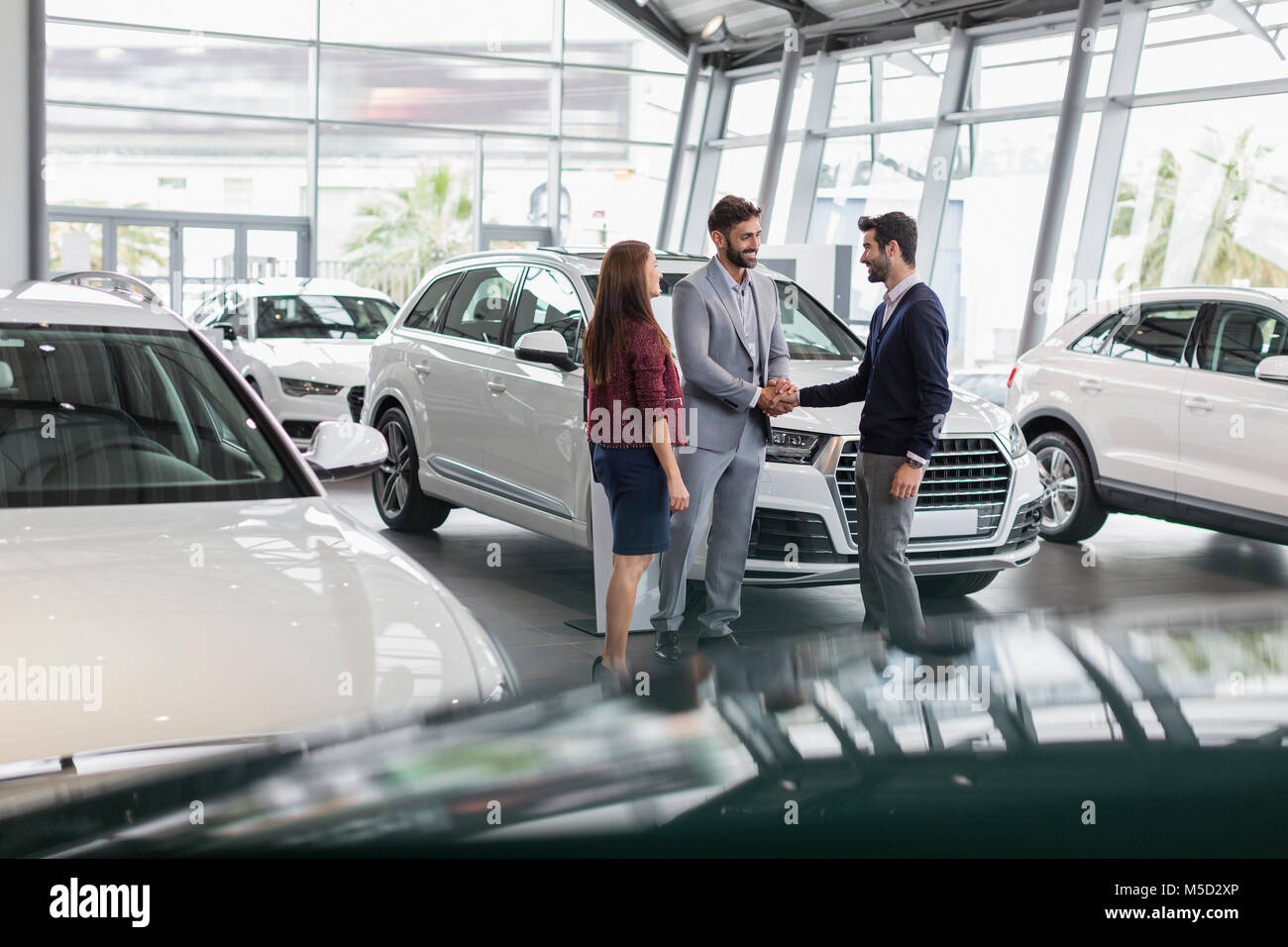 Car salesman and customers handshaking in car dealership showroom Stock Photo
