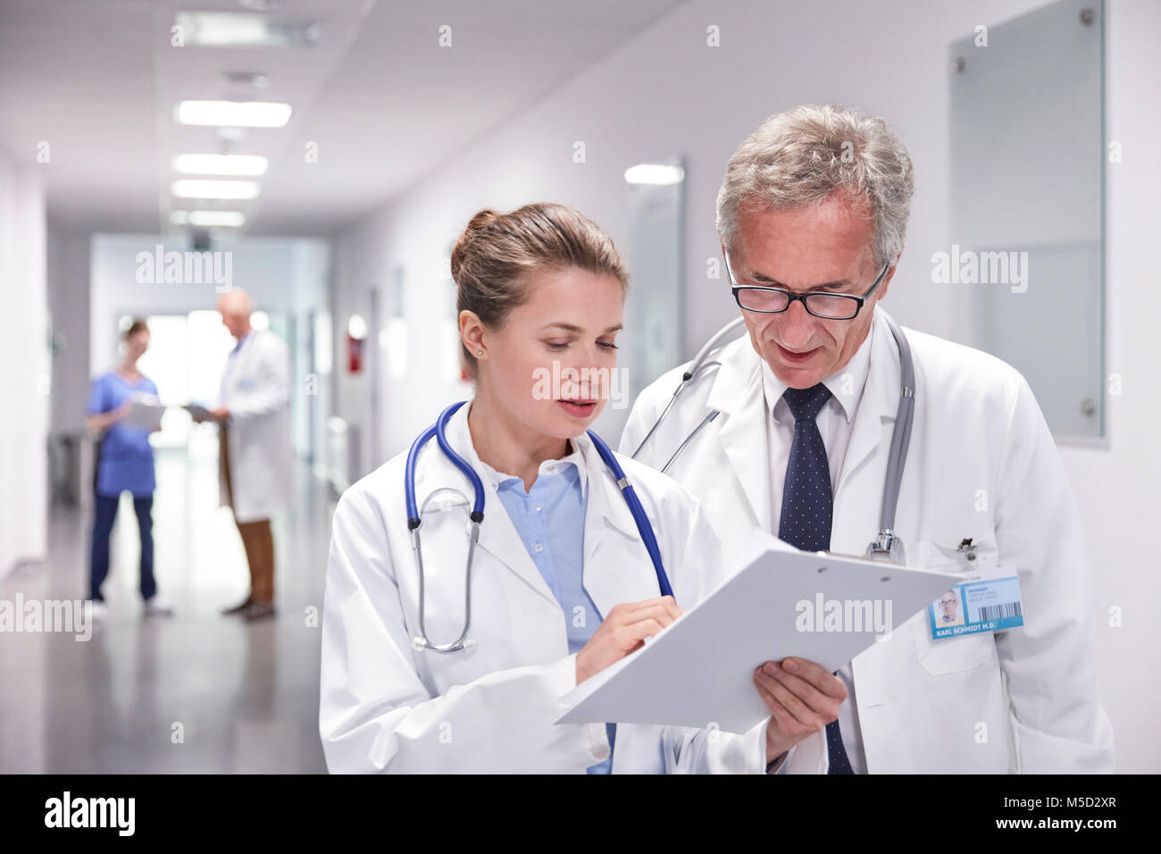 Doctors with clipboard making rounds, talking in hospital corridor Stock Photo