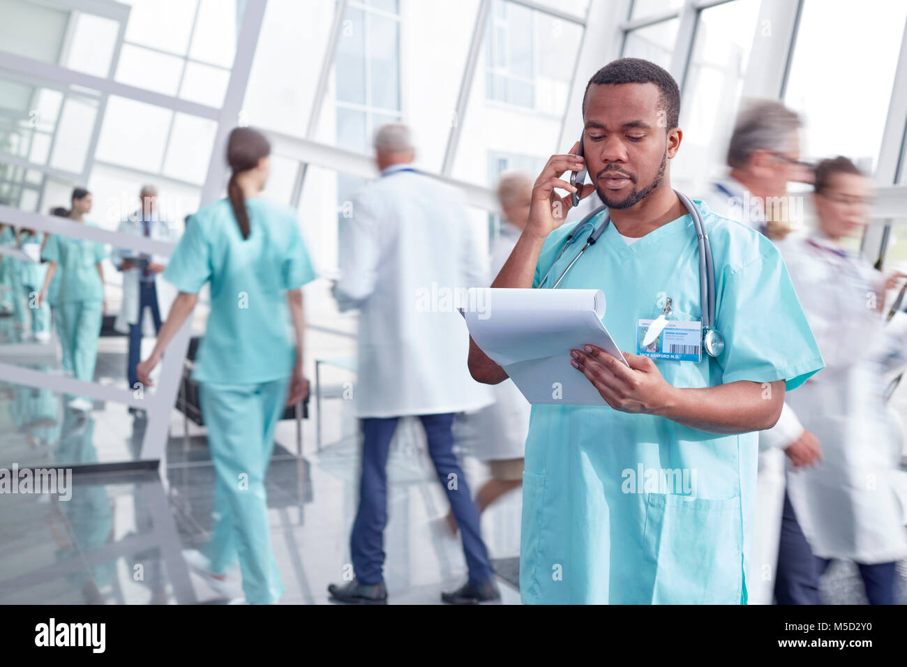 Male surgeon with clipboard talking on cell phone in hospital lobby Stock Photo