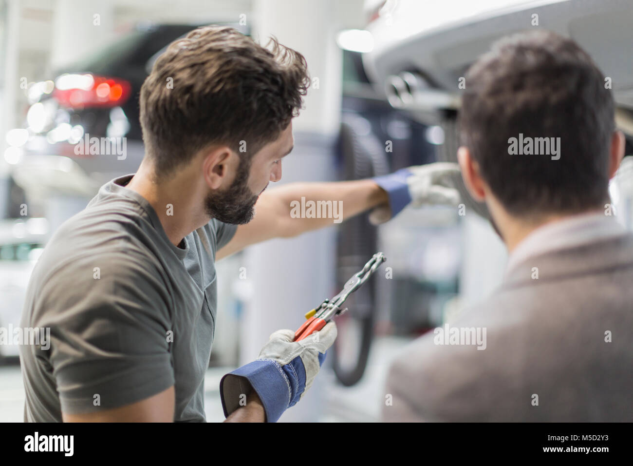 Auto mechanic with tool pointing, explaining to customer in auto repair shop Stock Photo