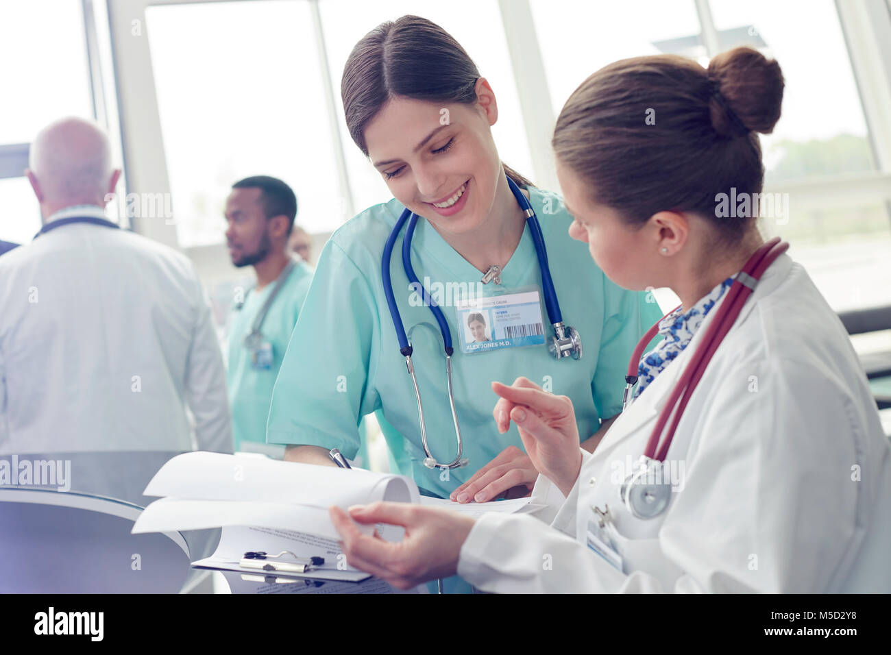 Smiling female doctor and nurse with clipboard talking in hospital Stock Photo
