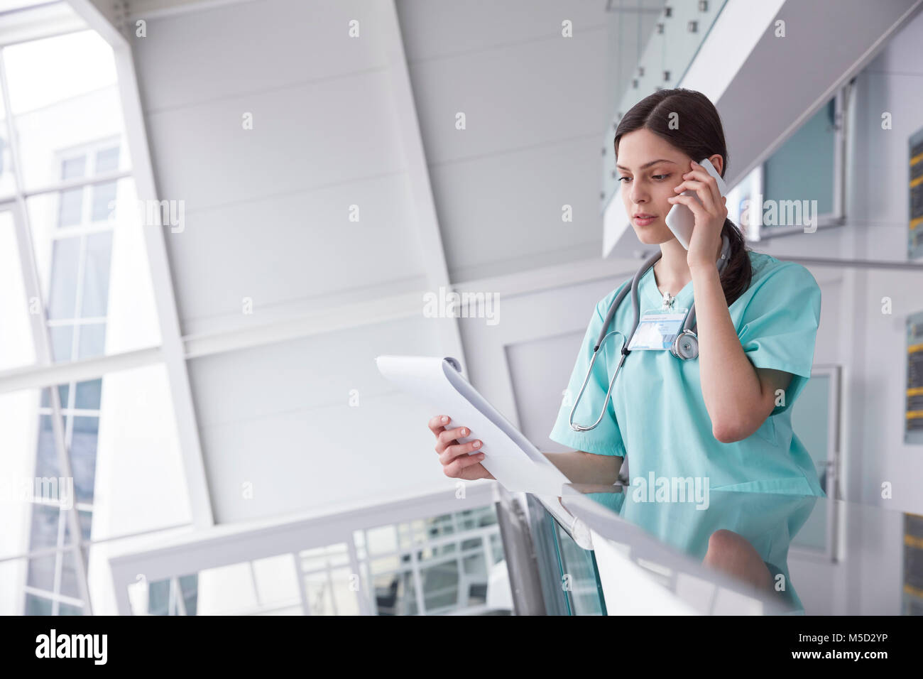 Female nurse with clipboard talking on cell phone in hospital Stock Photo
