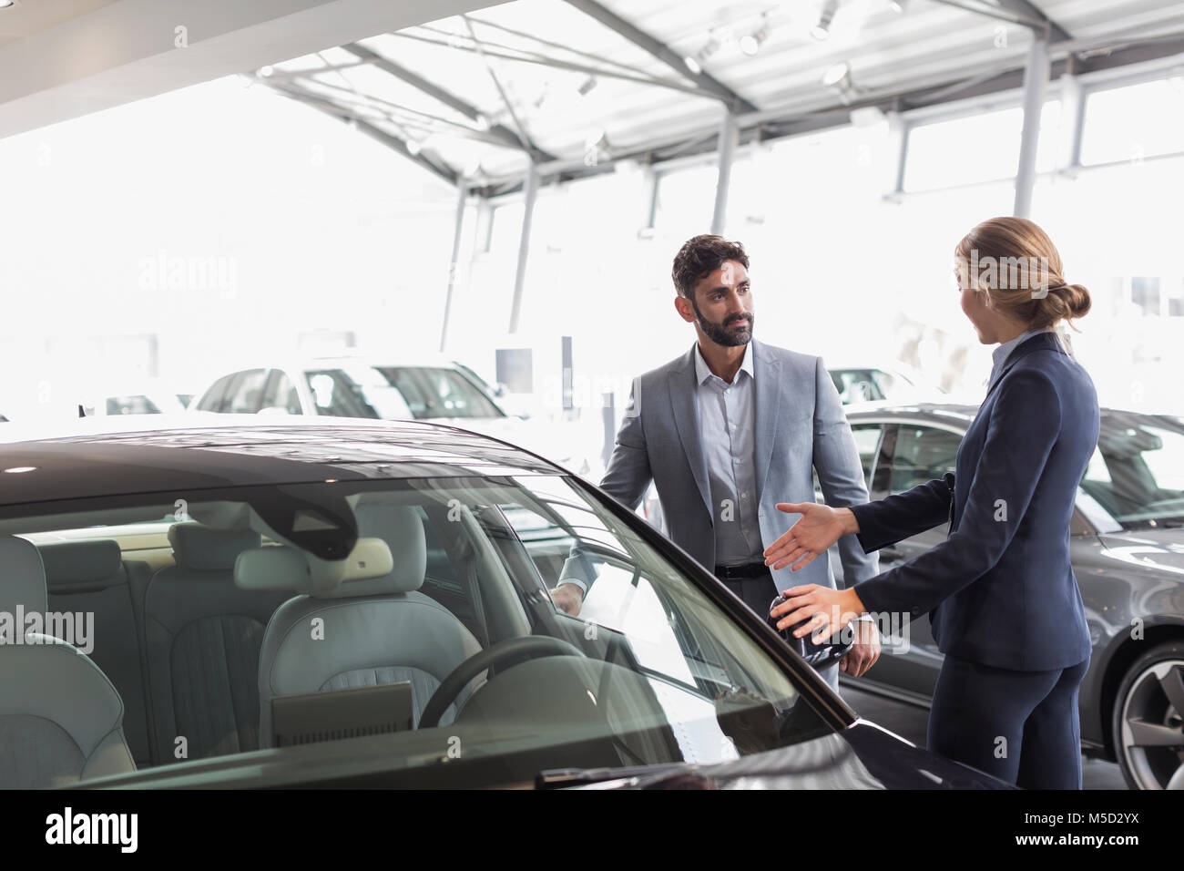 Car saleswoman showing new car to male customer in car dealership showroom Stock Photo