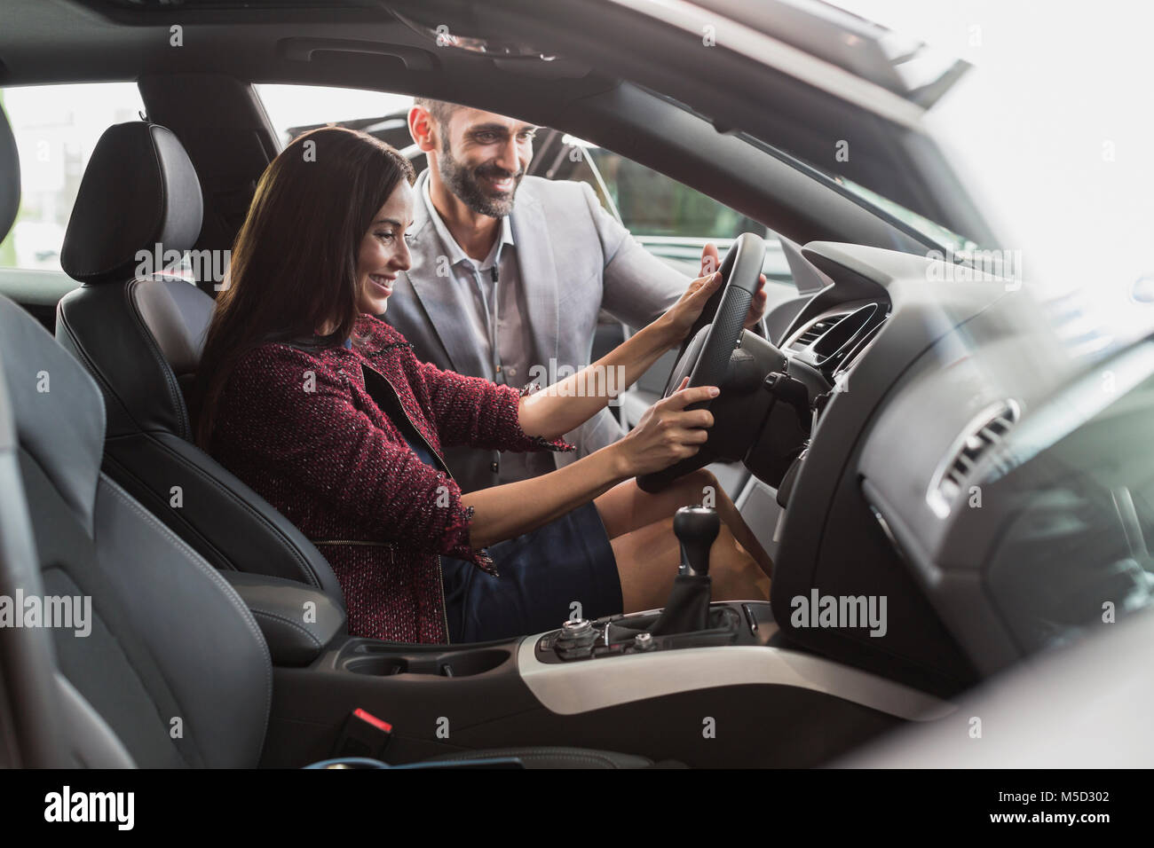 Car salesman and female customer in driver’s seat of new car in car dealership showroom Stock Photo