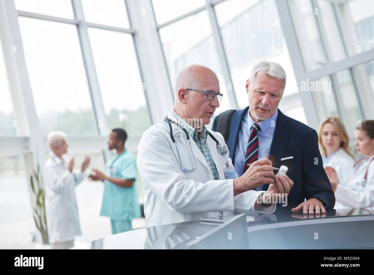 Male doctor and pharmaceutical representative discussing medication in hospital lobby Stock Photo